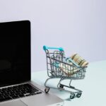Carrito de compra con dinero sobre un portátil, representando precios dinámicos en ecommerce con inteligencia artificial